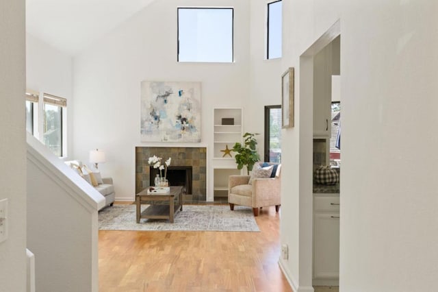 living room with light hardwood / wood-style flooring, a tiled fireplace, and high vaulted ceiling