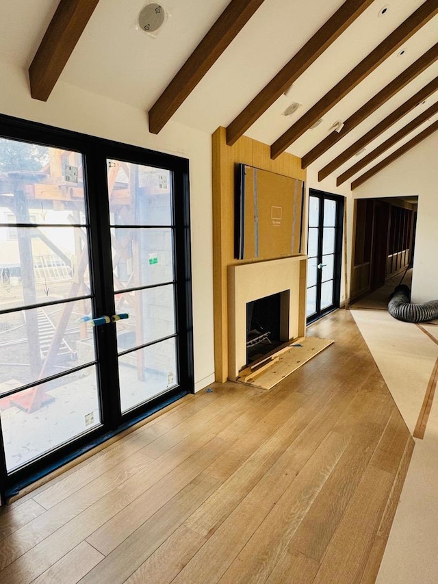 unfurnished living room featuring lofted ceiling with beams, light wood-type flooring, and french doors