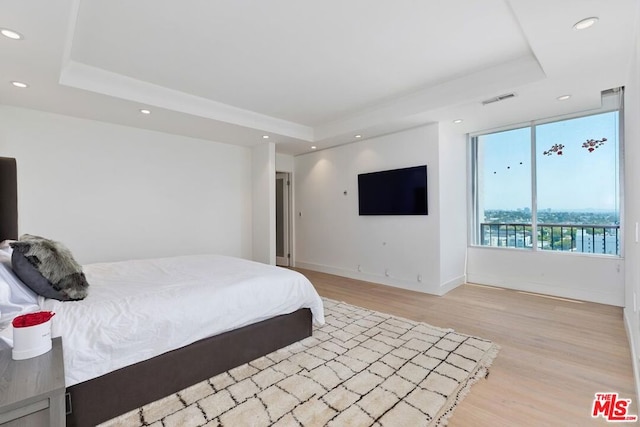 bedroom with a tray ceiling and light wood-type flooring