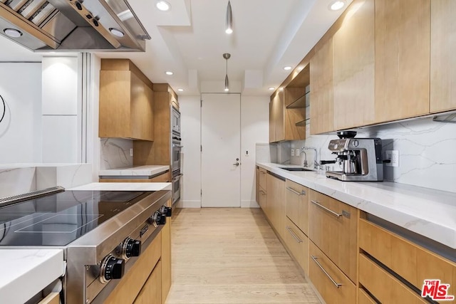 kitchen featuring appliances with stainless steel finishes, decorative backsplash, wall chimney range hood, light stone counters, and sink