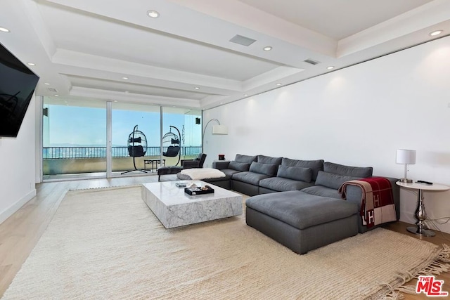 living room with a wall of windows, a tray ceiling, and light hardwood / wood-style floors