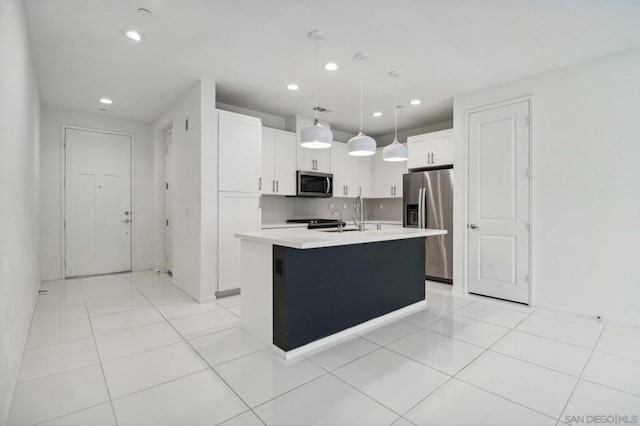 kitchen with pendant lighting, a center island with sink, light tile patterned floors, appliances with stainless steel finishes, and white cabinetry