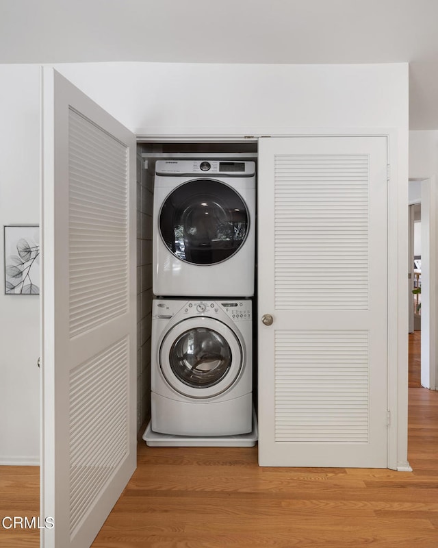 laundry room featuring wood-type flooring and stacked washer / drying machine