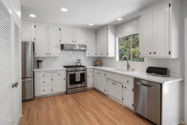 kitchen featuring wall chimney range hood, sink, appliances with stainless steel finishes, and light hardwood / wood-style flooring