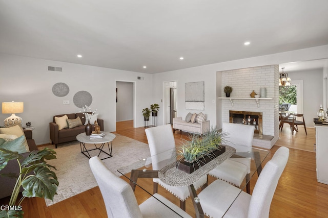 dining space featuring light wood-type flooring, a brick fireplace, and a notable chandelier