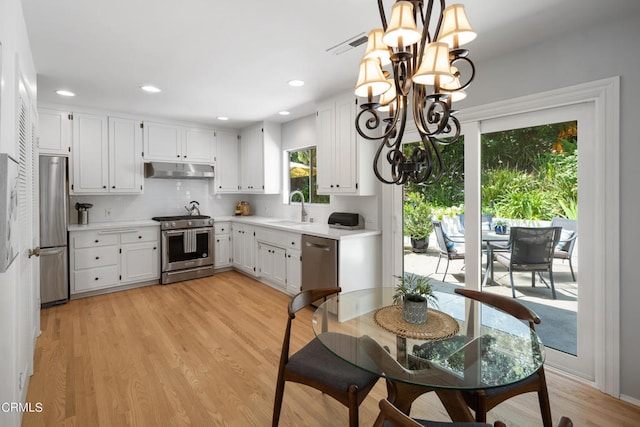 kitchen featuring appliances with stainless steel finishes, sink, light wood-type flooring, white cabinetry, and a notable chandelier