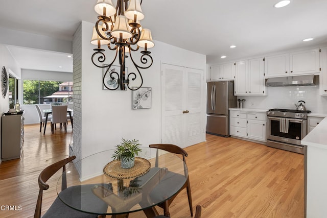 kitchen featuring decorative backsplash, white cabinets, light wood-type flooring, an inviting chandelier, and appliances with stainless steel finishes