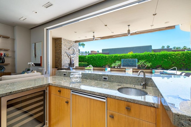 kitchen featuring wine cooler, sink, light stone counters, and ceiling fan