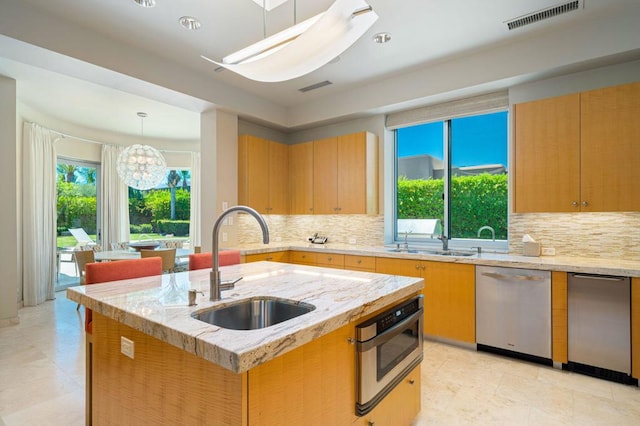 kitchen featuring decorative backsplash, stainless steel appliances, a center island with sink, sink, and a chandelier