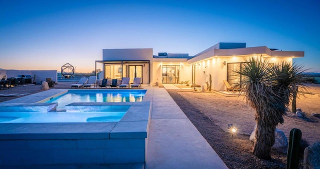 pool at dusk featuring a patio area and an in ground hot tub