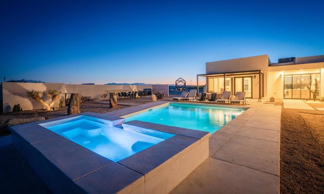 pool at dusk featuring an in ground hot tub and a patio area