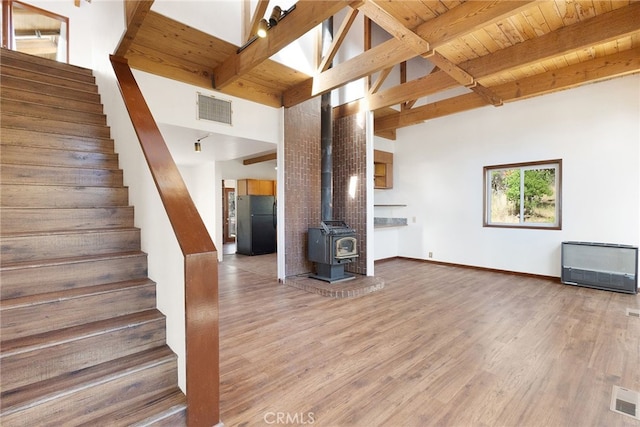 unfurnished living room featuring beam ceiling, a wood stove, a high ceiling, and hardwood / wood-style flooring