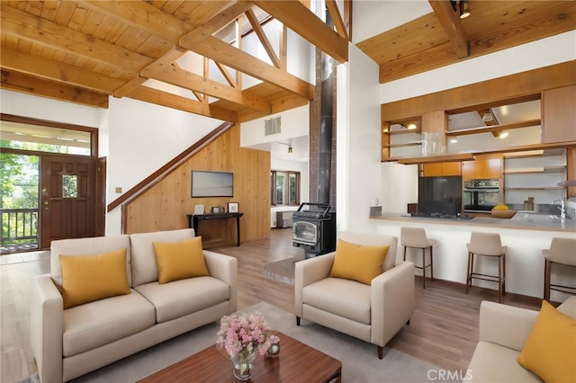 living room with beamed ceiling, a towering ceiling, a wood stove, and wooden walls