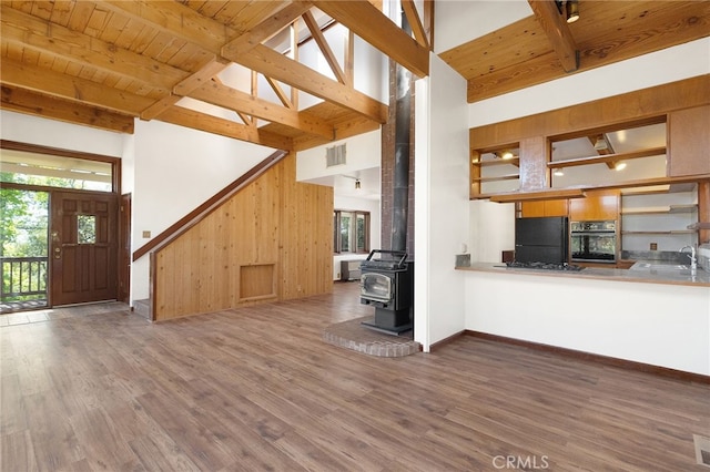 kitchen featuring black appliances, kitchen peninsula, a towering ceiling, and a wood stove