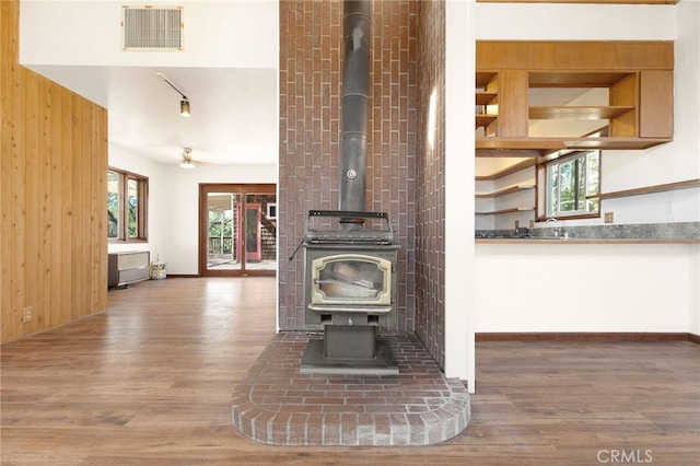 room details with hardwood / wood-style floors, ceiling fan, a wood stove, and wooden walls