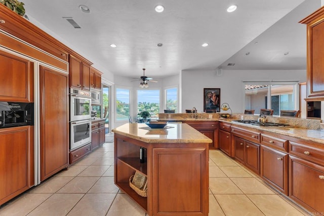 kitchen featuring a center island, light stone countertops, ceiling fan, appliances with stainless steel finishes, and light tile patterned flooring