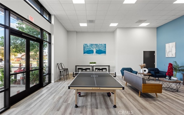 playroom featuring a towering ceiling, french doors, light hardwood / wood-style floors, and a drop ceiling