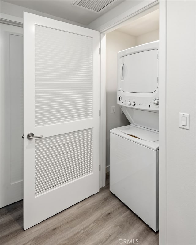 laundry area with stacked washer / dryer and hardwood / wood-style flooring