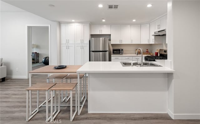 kitchen with light hardwood / wood-style floors, kitchen peninsula, white cabinetry, appliances with stainless steel finishes, and sink