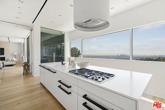 kitchen featuring sink, light hardwood / wood-style flooring, a healthy amount of sunlight, white cabinetry, and stainless steel gas cooktop