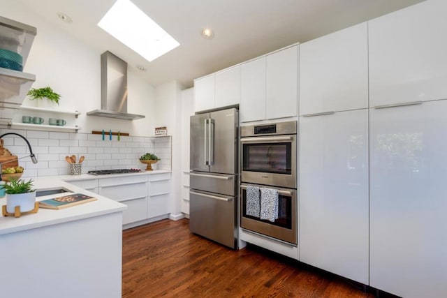 kitchen featuring appliances with stainless steel finishes, sink, white cabinetry, and wall chimney range hood