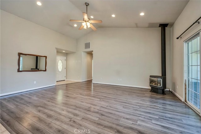 unfurnished living room with a wood stove, high vaulted ceiling, light hardwood / wood-style flooring, and ceiling fan