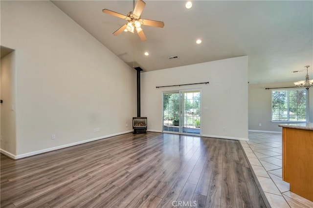 unfurnished living room featuring high vaulted ceiling, light hardwood / wood-style floors, a wood stove, and a wealth of natural light