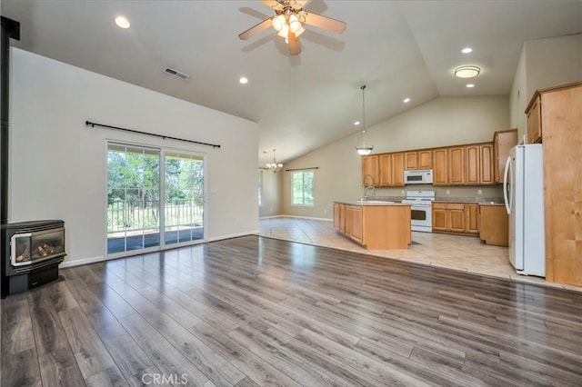 kitchen with a center island with sink, white appliances, a wood stove, and a wealth of natural light