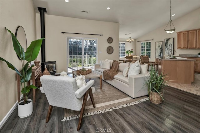 living room with a notable chandelier, lofted ceiling, hardwood / wood-style floors, and a wood stove