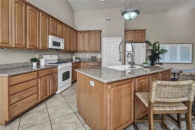 kitchen featuring light tile patterned flooring, sink, a center island with sink, white appliances, and light stone countertops