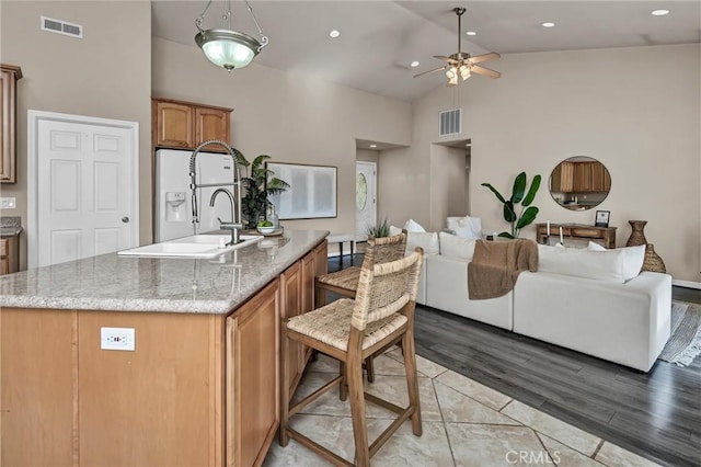 kitchen featuring sink, a kitchen island with sink, high vaulted ceiling, light stone counters, and light hardwood / wood-style floors