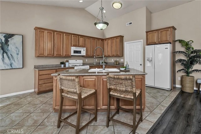 kitchen with a breakfast bar, pendant lighting, sink, a kitchen island with sink, and white appliances