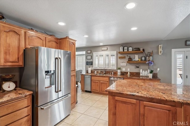 kitchen featuring sink, a textured ceiling, light tile patterned flooring, light stone counters, and stainless steel appliances