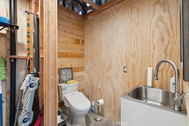 bathroom with wood walls, toilet, and sink