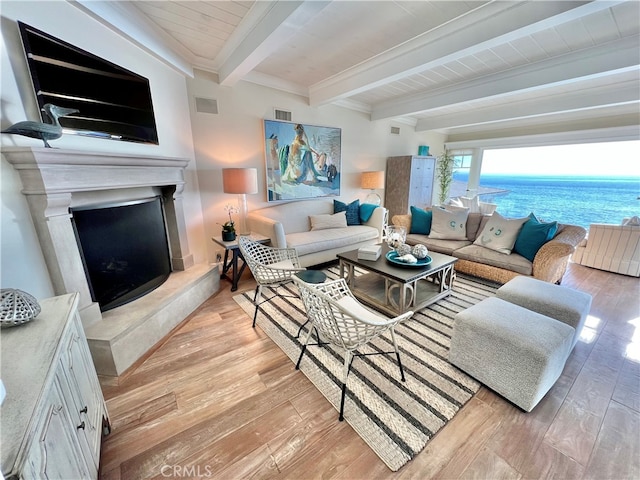 living room with a fireplace, a water view, beam ceiling, and light wood-type flooring