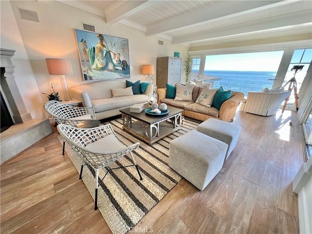 living room with beam ceiling, a fireplace, light hardwood / wood-style floors, and a water view