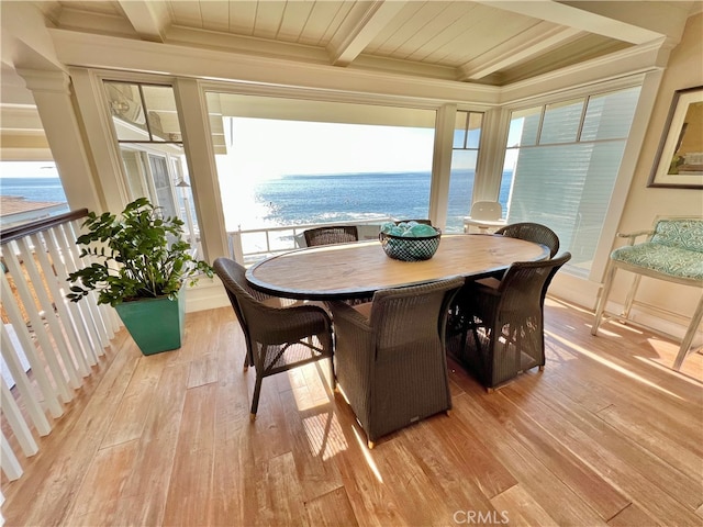 dining area featuring ornamental molding, a water view, beam ceiling, and light wood-type flooring