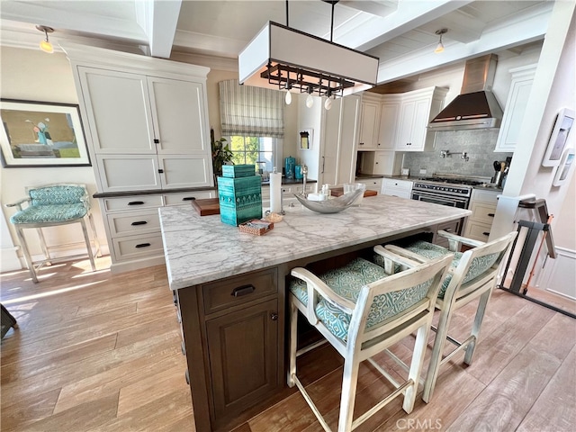 kitchen with pendant lighting, beamed ceiling, a kitchen island, and wall chimney range hood