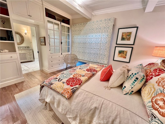 bedroom with beamed ceiling, connected bathroom, light hardwood / wood-style floors, and ornamental molding