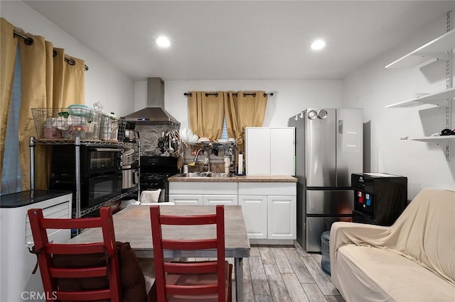 kitchen featuring a sink, light wood-style flooring, white cabinets, wall chimney exhaust hood, and gas stove