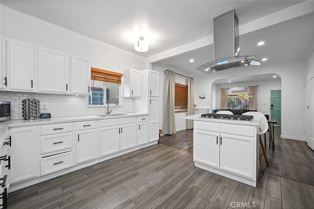 kitchen featuring gas cooktop, island exhaust hood, a sink, dark wood-style flooring, and decorative backsplash