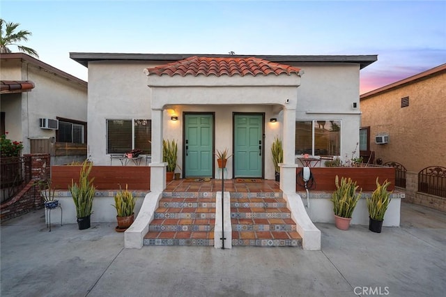 mediterranean / spanish home with fence, a tile roof, a wall mounted air conditioner, and stucco siding