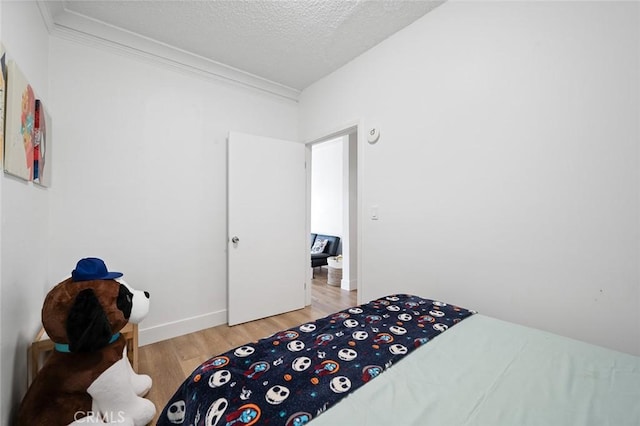 bedroom featuring light wood-style flooring, a textured ceiling, and ornamental molding