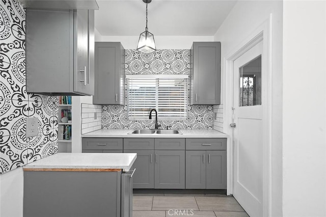 kitchen with light countertops, backsplash, gray cabinets, and a sink