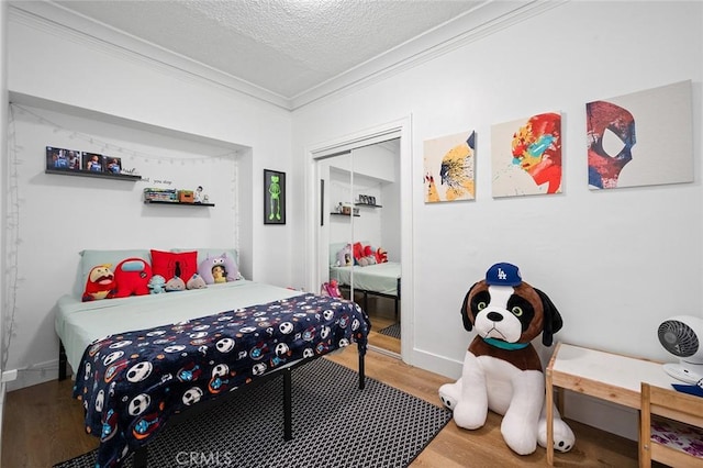 bedroom with crown molding, wood finished floors, a textured ceiling, a closet, and baseboards