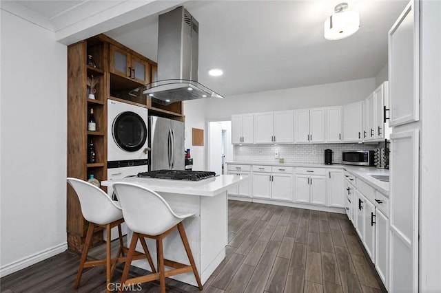 kitchen with stainless steel appliances, a kitchen breakfast bar, island exhaust hood, dark wood-style floors, and stacked washer / dryer