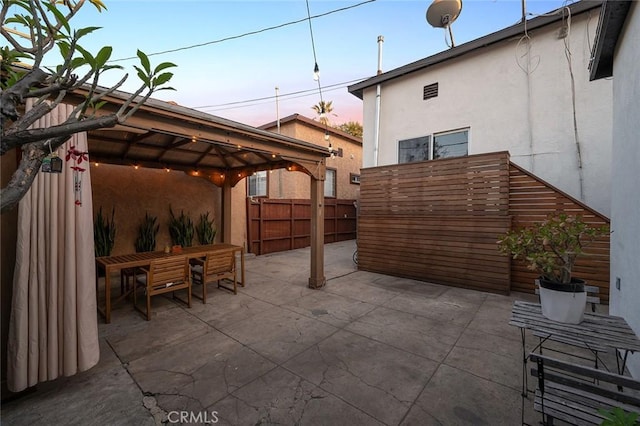 patio terrace at dusk featuring a gazebo, fence, and outdoor dining space