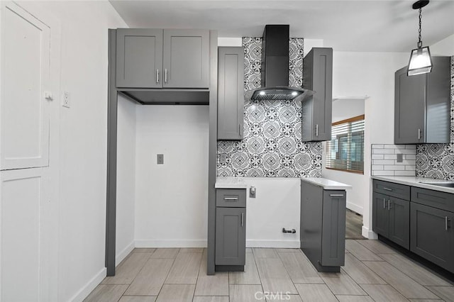 kitchen featuring backsplash, light countertops, wall chimney range hood, and gray cabinetry