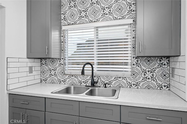 kitchen with light countertops, gray cabinets, decorative backsplash, and a sink