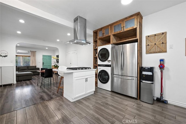 kitchen with island exhaust hood, arched walkways, freestanding refrigerator, wood finished floors, and stacked washing maching and dryer
